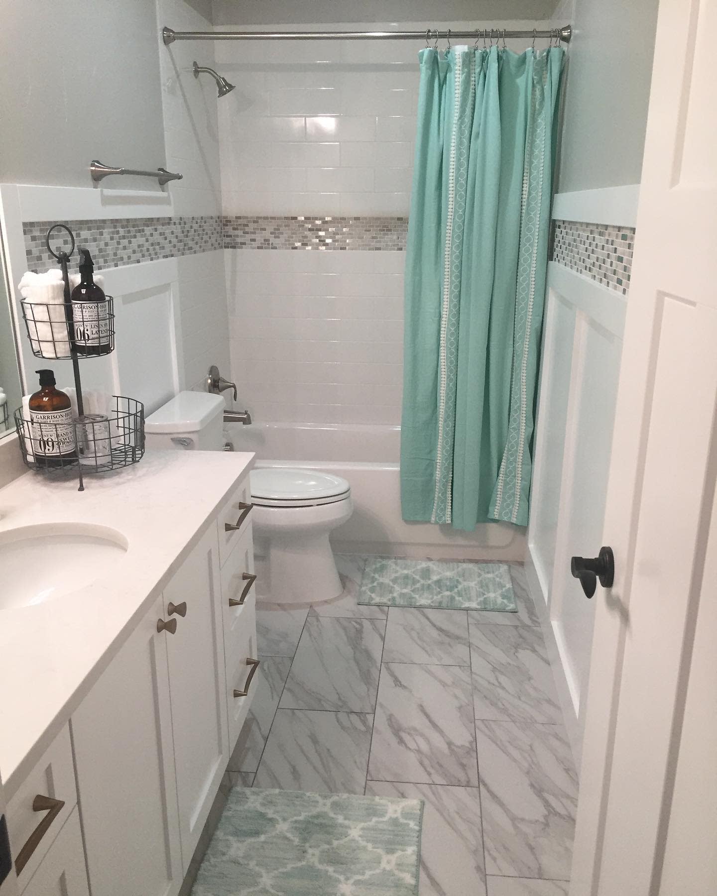 Bathroom with marble tile floor, white vanity, and aqua shower curtain.